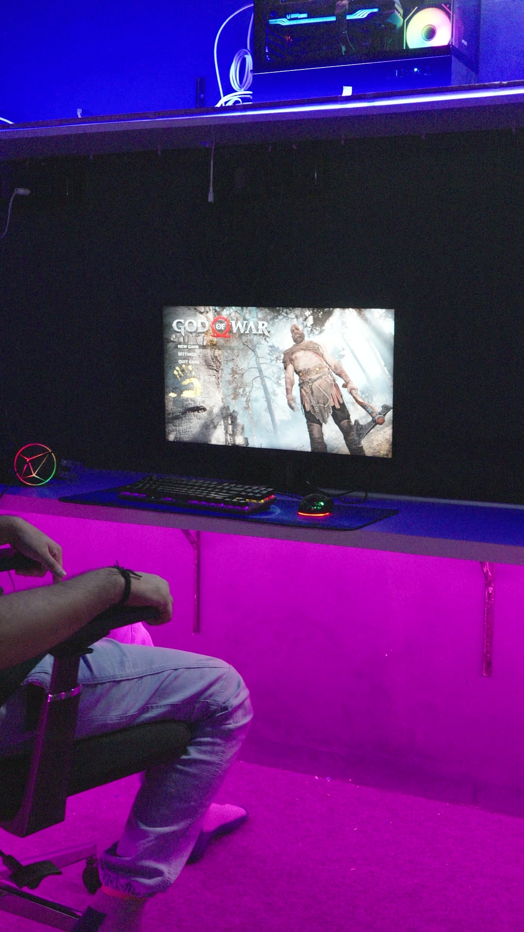 A gaming PC desk glowing pink with a game on the monitor